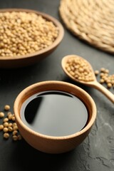 Tasty soy sauce in bowl and soybeans on black table, closeup