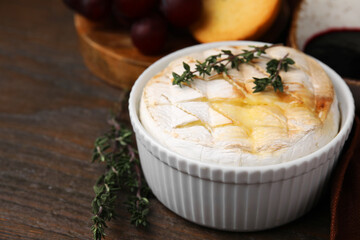 Tasty baked camembert and thyme in bowl on wooden table, closeup. Space for text