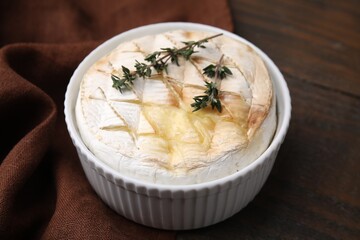 Tasty baked camembert and thyme in bowl on wooden table, closeup
