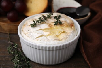 Tasty baked camembert and thyme in bowl on wooden table, closeup