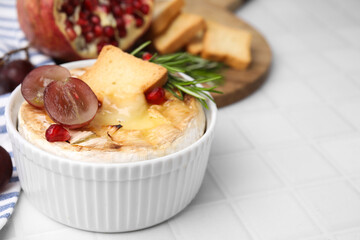 Tasty baked camembert with crouton, grape and rosemary on white tiled table, closeup. Space for text