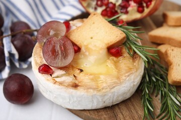Tasty baked camembert with crouton, grape and rosemary on white tiled table, closeup