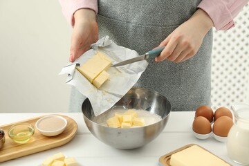 Woman adding fresh butter into bowl with flour at white table, closeup