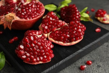 Cut fresh pomegranate and green leaves on grey table, closeup