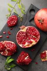 Fresh pomegranates and green leaves on grey table, top view