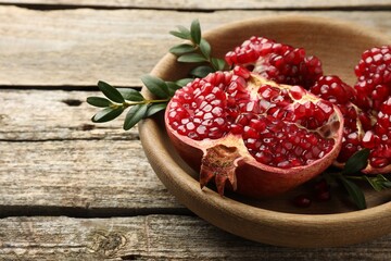 Cut fresh pomegranate and green leaves on wooden table, closeup. Space for text