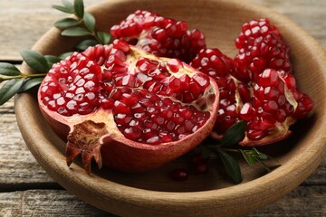 Cut fresh pomegranate and green leaves on wooden table, closeup