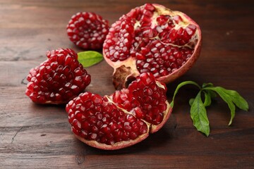 Cut fresh pomegranate and green leaves on wooden table, closeup