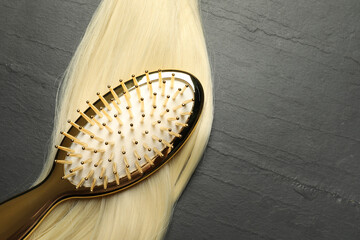 Stylish brush with blonde hair strand on dark grey table, top view. Space for text