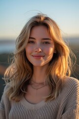 A young woman with long, wavy blonde hair is smiling at the camera. She is wearing a tan sweater.
