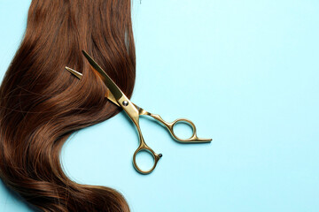 Professional hairdresser scissors with brown hair strand on light blue background, top view. Space...