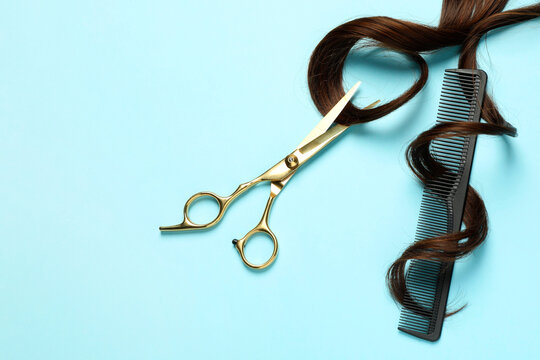 Professional hairdresser scissors and comb with brown hair strand on light blue background, flat lay. Space for text