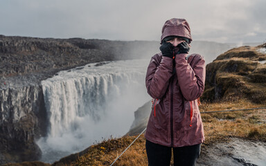 Young hiker in front of a large waterfall. Red windbreaker, technical raincoat. Adventure, travel, cold.