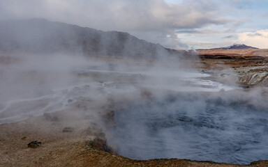 Námafjall Geothermal Area. Tourists in the distance, steaming fumaroles, boiling mud pots. Panorama of suggestive volcanic landscape. Sulfurous springs, solfataras and steam springs.