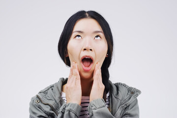 Asian woman, portrait and shocked on studio background for wow with crazy expression, social media and hands. Female person, surprise and grey backdrop with omg face for gossip, secret drama and wtf