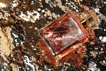 Luxury perfume in bottle on fabric with silver sequins, top view