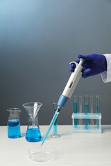 Laboratory analysis. Scientist dripping sample with micropipette into petri dish at white wooden...