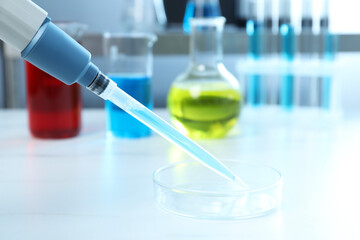 Laboratory analysis. Micropipette with liquid and petri dish on white table, closeup