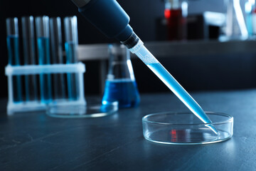 Laboratory analysis. Micropipette with liquid and petri dish on black table