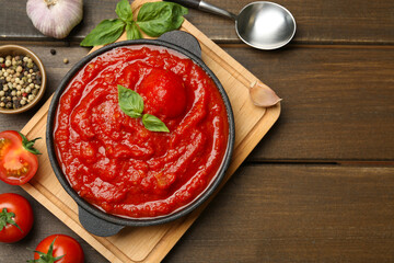 Homemade tomato sauce in bowl, spoon and ingredients on wooden table, flat lay. Space for text