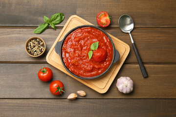 Homemade tomato sauce in bowl, spoon and ingredients on wooden table, flat lay