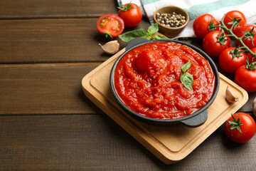 Homemade tomato sauce in bowl and ingredients on wooden table, space for text