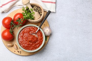 Homemade tomato sauce in bowl, spoon and fresh ingredients on light grey table, flat lay. Space for...