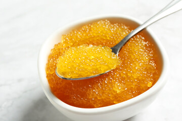 Fresh pike caviar in bowl and spoon on white table, closeup
