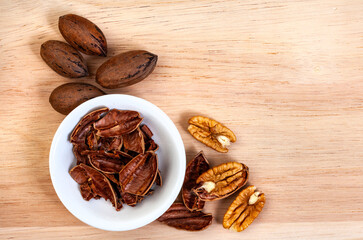 Whole and shelled pecan nuts on light wooden surface with copy space
