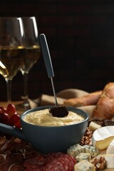 Fondue pot with tasty melted cheese, fork, different snacks and wine on table