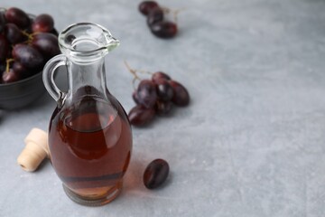 Wine vinegar in glass jug and grapes on grey table, space for text