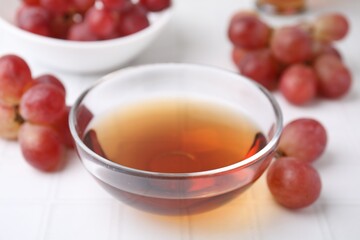 Wine vinegar in glass bowl and grapes on white table, closeup