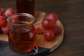 Wine vinegar in glass jar and grapes on wooden table, closeup