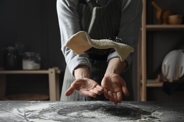 Woman tossing pizza dough at table in kitchen, closeup