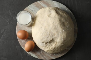 Raw dough, eggs and milk on black table, top view