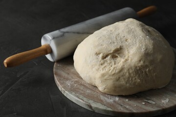 Raw dough and rolling pin on black table, closeup