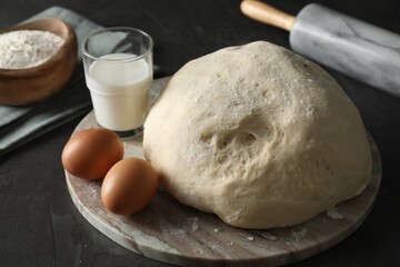 Raw dough, rolling pin and ingredients on black table