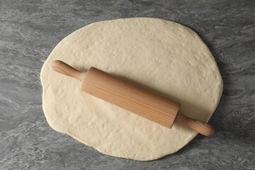 Raw dough and rolling pin on grey table, top view