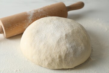 Raw dough and rolling pin on table