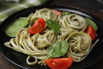 Tasty pasta with spinach, sauce and tomatoes on table, closeup