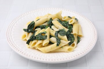 Tasty pasta with spinach and sauce on white tiled table