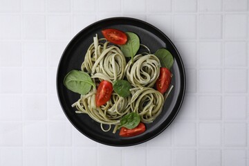 Tasty pasta with spinach, sauce and tomatoes on white tiled table, top view