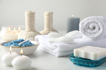 Spa composition. Towels, herbal bags, soap, sea salt and burning candles on light table