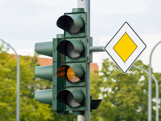 Traffic light blinking yellow and priority road sign next to it. The light signal is broken of...