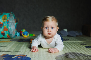 Fototapeta premium A four-month-old boy lies on the floor on a rug and plays with toys. The child holds his head. A baby learns to crawl on the floor