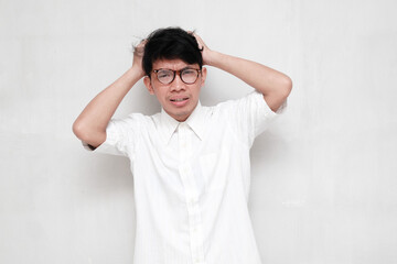 A young Asian man wearing a white shirt and glasses feels dizzy or stressed. Isolated white...