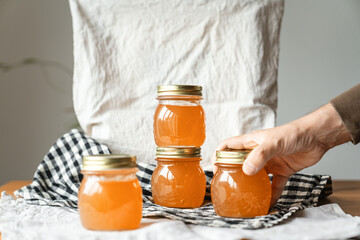 Marmelade hausgemacht zu Hause in Einmachgläsern zur präsentation auf dem Tisch auf kariertem Tuch Gelee und eine Hand die nach einem Glas reicht