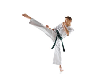 Teen boy, athlete practices karate moves, demonstrating skills and determination, practicing isolated on white studio background. Concept of sport, martial arts, combat sport, active lifestyle © master1305