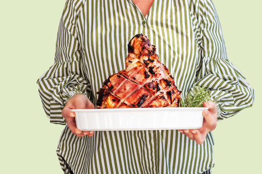 woman holding baked christmas ham, against a light pistachio green background