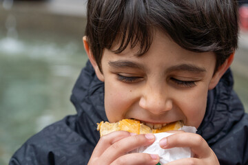 Kid eating street food lunch outdoors, bitting a sandwich.
